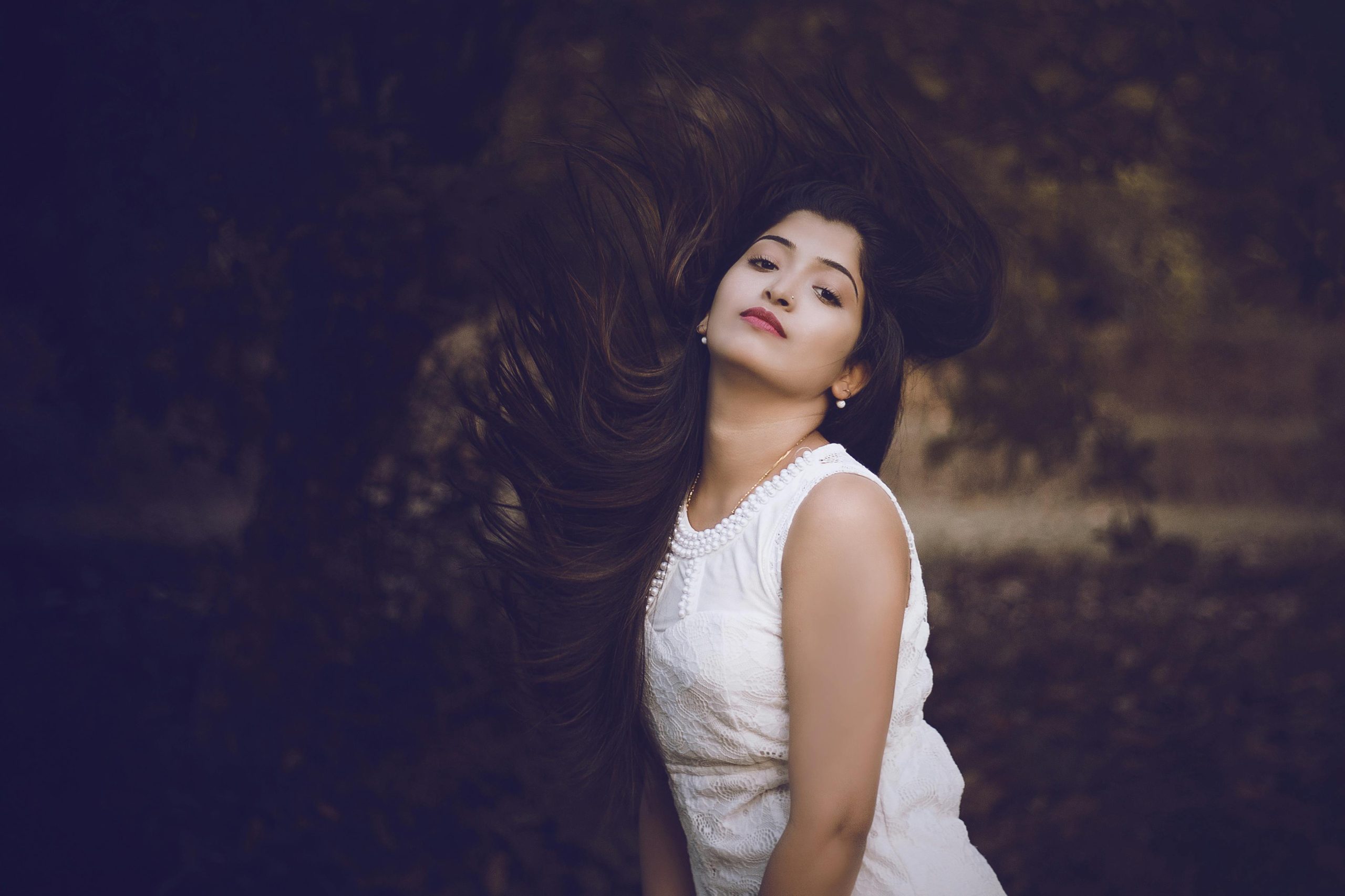 Striking portrait of a woman with flowing hair wearing a white dress in a natural setting.